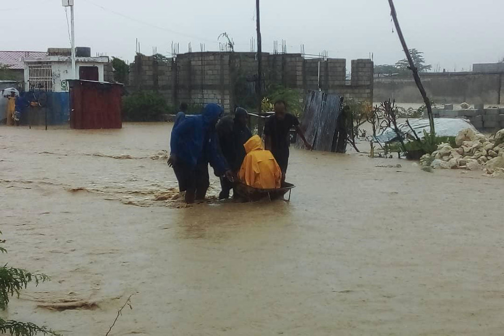 Watu waliovaa makoti ya mvua wanamsukuma mtu aliye kwenye toroli kupitia barabara iliyojaa maji nchini Haiti.