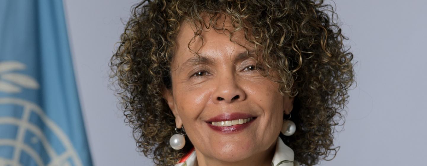 Cristina Duarte, Conselheira Especial para a África do Secretário-Geral das Nações Unidas , sorri durante uma sessão de fotos com a bandeira da ONU ao fundo.
