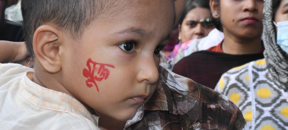 A young boy with the Bangla word for 'free' written on his cheek is carried by an adult at a recent demonstration in Bangladesh.