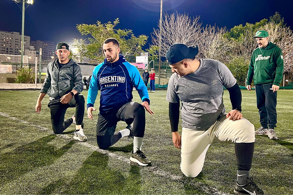 El beisbolista venezolano Carlos Jiménez calienta con sus compañeros de la Selección Nacional de Béisbol de Argentina por la noche.