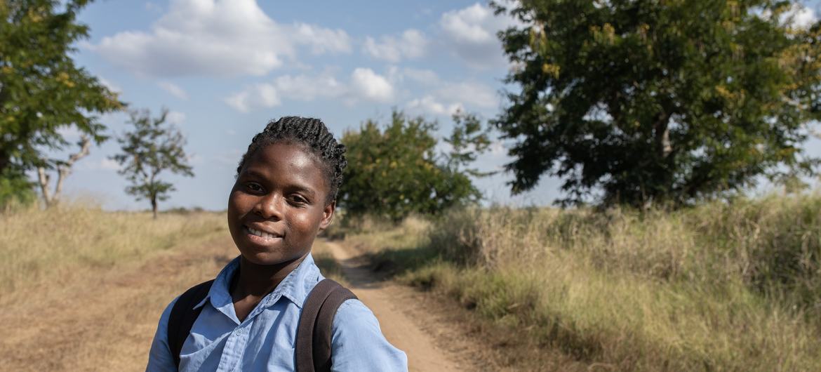 A estudante moçambicana Margarida Joaquim Oio Oio está em uma estrada de terra segurando cadernos, a caminho de casa após as aulas no distrito de Buzi, província de Sofala.