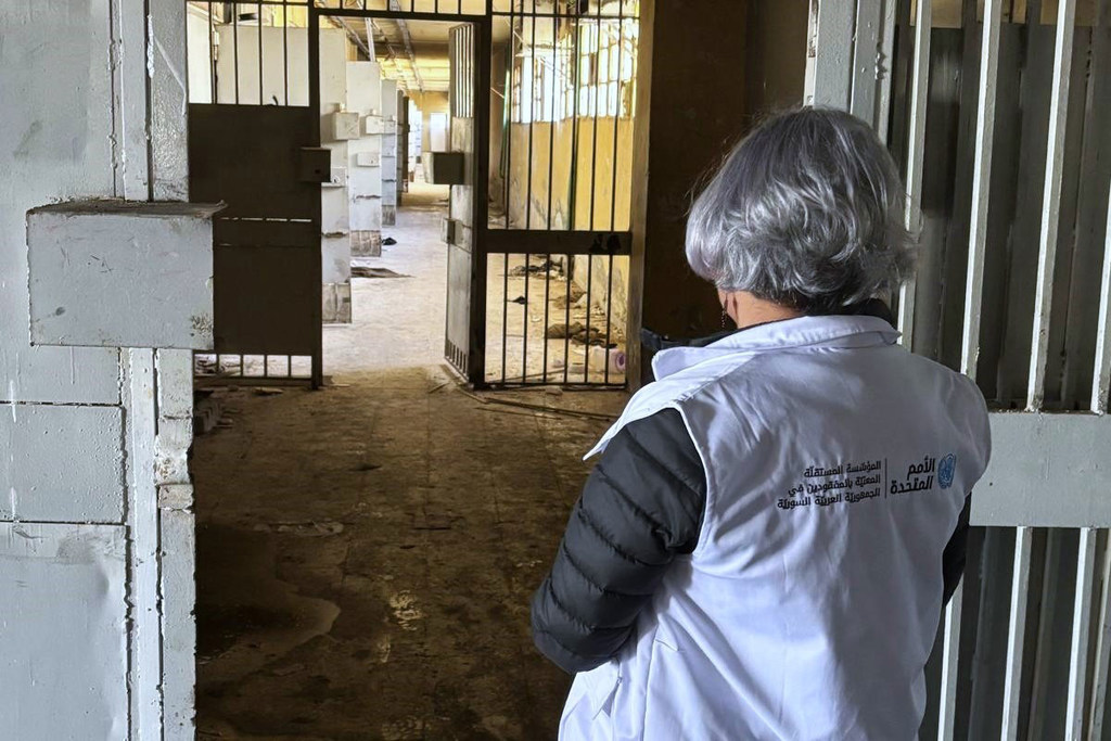 Mme Karla Quintana, directrice de l'Institution indépendante pour les personnes disparues en République arabe syrienne, vêtue d'un gilet de ONU , se tient devant une grille et regarde à l'intérieur d'un bâtiment en béton.