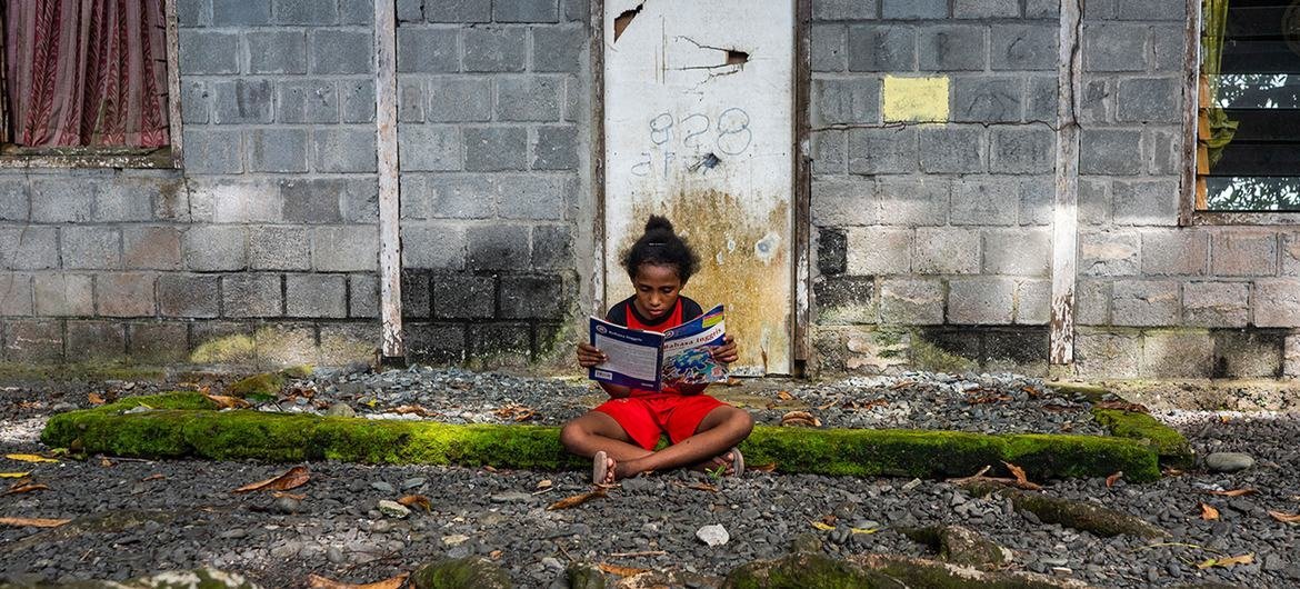 Uma menina lê um livro em frente à sua casa em Papua, uma das províncias mais pobres da Indonésia