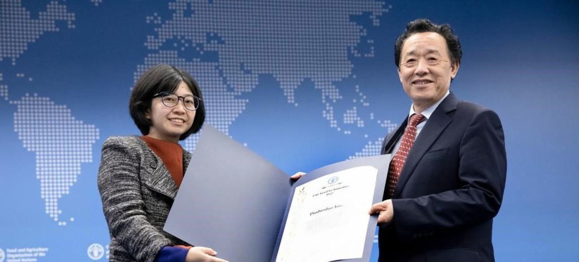 在一个以世界地图为背景的蓝色背景的活动上，一名女子和一名男子共同拿着一张证书。