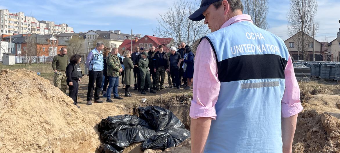 A UN staffer stands in front of a mass grave site in Bucha, Ukraine. In the background the United Nations Emergency Relief Coordinator Martin Griffiths.