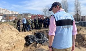 A UN staffer stands in front of a mass grave site in Bucha, Ukraine. In the background the United Nations Emergency Relief Coordinator Martin Griffiths.