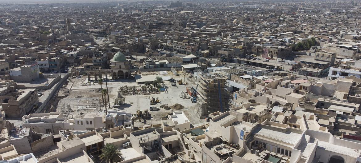 صورة جوية لمدينة الموصل في العراق، تُظهر جهود إعادة الإعمار والترميم الحضري، مع مبنى يتميز بقبة خضراء ومواقع بناء وسط أسطح منازل المدينة.