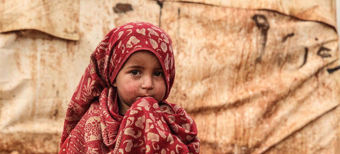 A young girl in a red patterned headscarf looks to the camera at the Khair Al-Sham IDP camp in Idleb Governorate, west of the town of Sarmada.