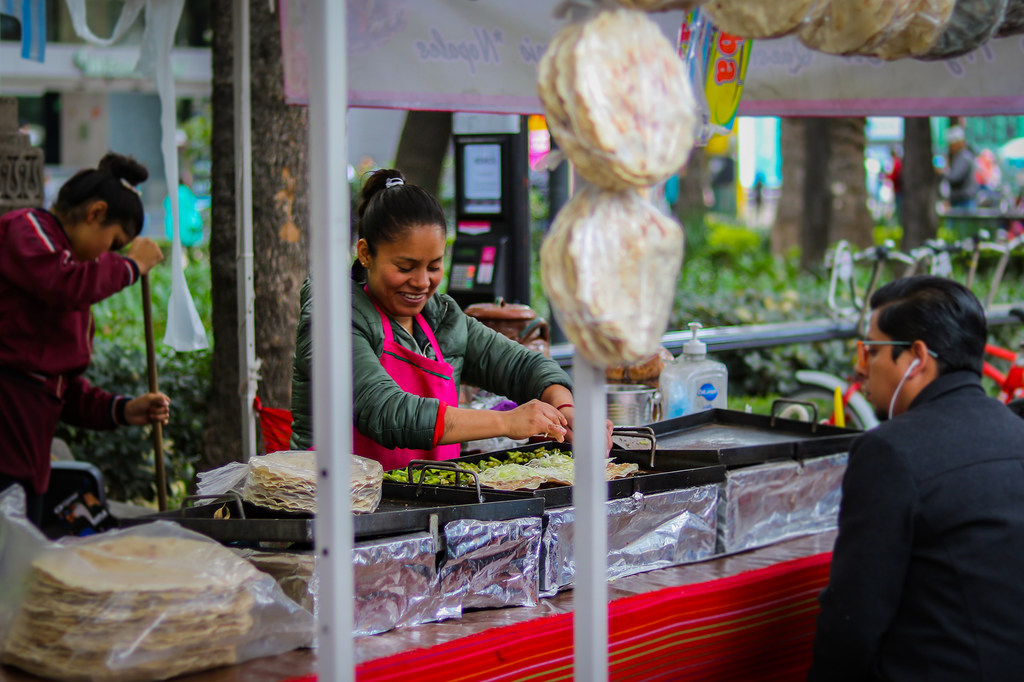 Una mujer sonríe mientras prepara tortillas en un puesto de comida callejera en la Ciudad de México.