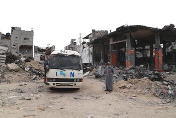 فلسطيني يقف  بجوار سيارة تابعة للأمم المتحدة ومبنى طالهما الدمار في غزة.