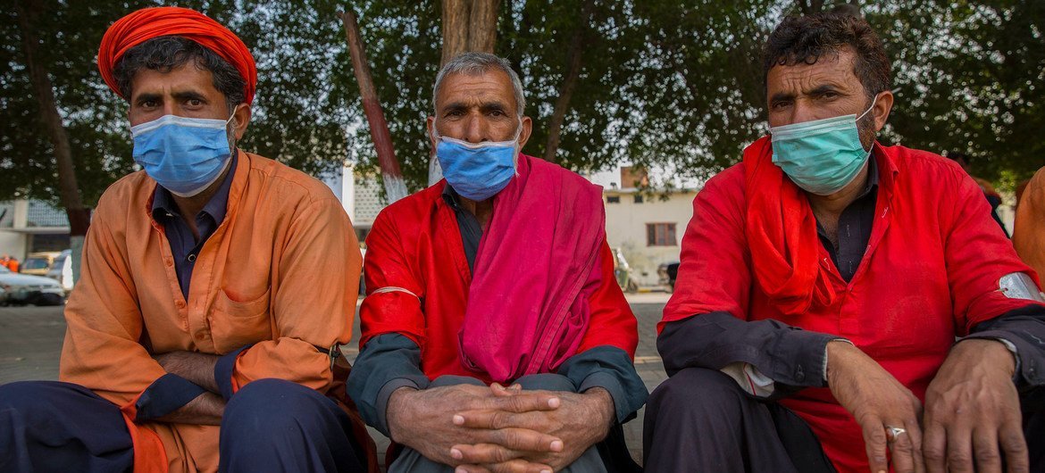 Men sit on the sidewalk in Pakistan waiting to be hired for work.