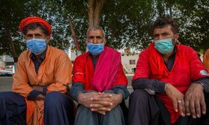 Men sit on the sidewalk in Pakistan waiting to be hired for work.