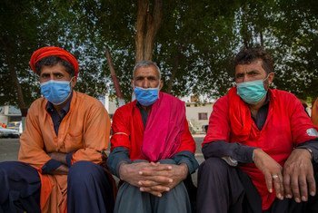 Men sit on the sidewalk in Pakistan waiting to be hired for work.