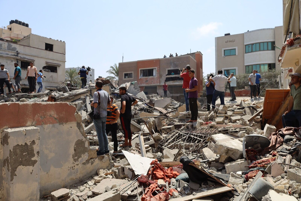 Pessoas estão em pé sobre os escombros de um prédio que desabou em Gaza, Palestina.