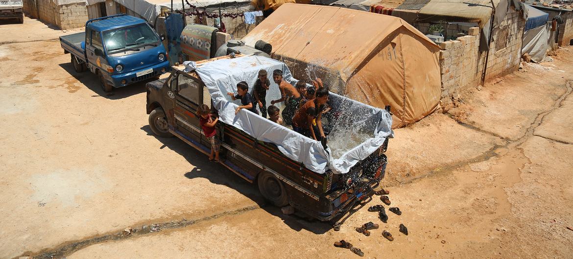 Em um campo para pessoas deslocadas pelo conflito no noroeste da Síria, crianças se refrescam das altas temperaturas do verão na traseira de um caminhão transformado em uma piscina temporária.