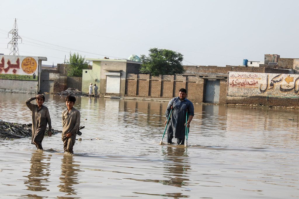 在巴基斯坦开伯尔-普赫图赫瓦省受灾最严重的地区之一瑙谢拉卡兰，两个男孩和一名拄着拐杖的男子穿过被洪水淹没的街道。