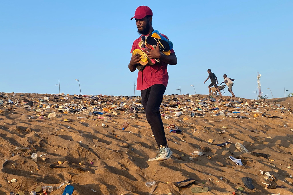 Aristide Kouame, un homme, traverse une plage de sable jonchée de détritus à Abidjan, tenant une collection de tongs.