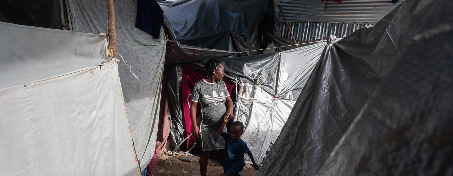 Une femme marche avec ses enfants entre plusieurs tentes à l'intérieur du site de déplacement de l'école Jean Marie Césard, Route de Frères, à Port-au-Prince.