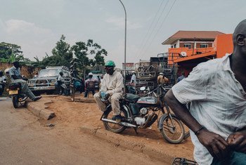 Men on motorcycles at a street scene in Kampala, Uganda. One man wears a green helmet and sits on a Yamaha motorcycle, while another sits on a curb nearby.