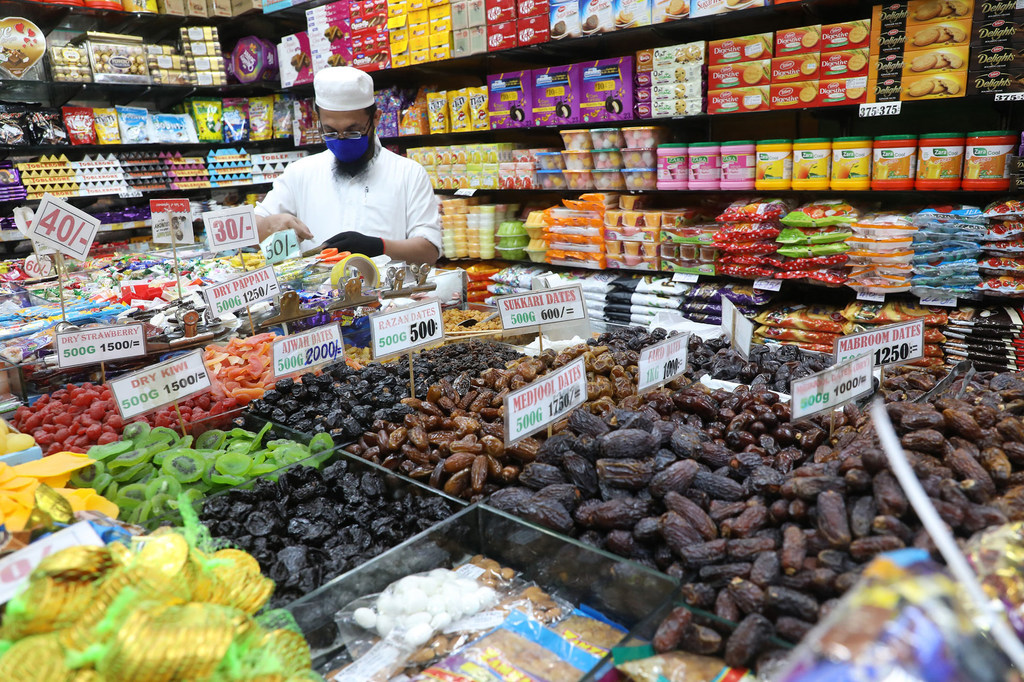 Un comerciante de Sri Lanka, con mascarilla y gorro blanco, coloca dátiles y dulces en una tienda de Colombo.