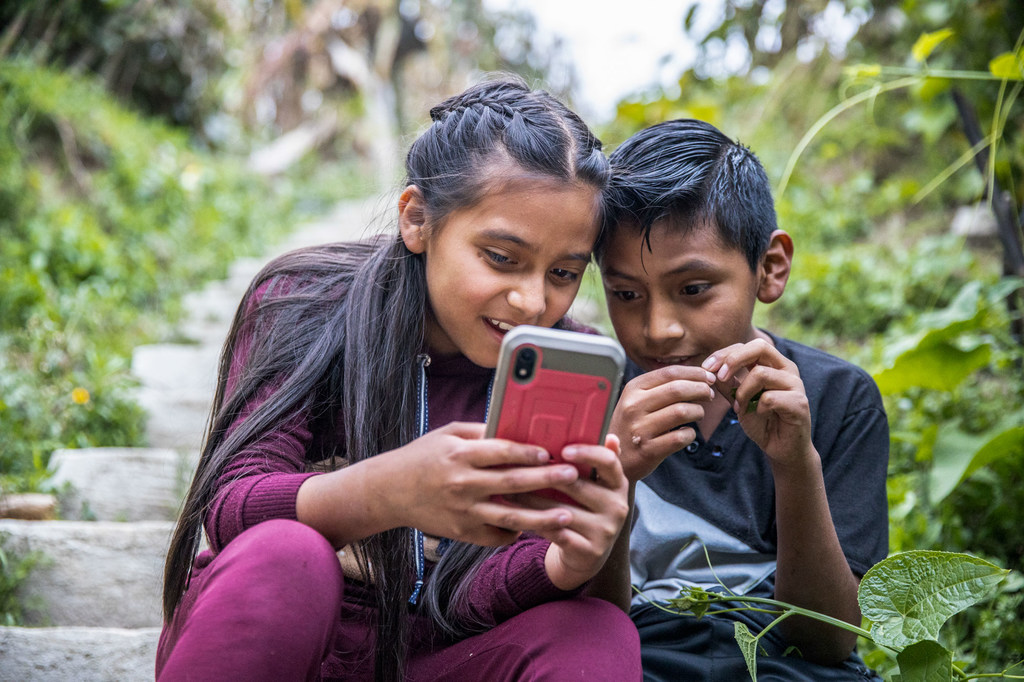 طفلان يلعبان في الخارج بينما يشارك والديهما في ورشة عمل حول الأمان عبر الإنترنت وممارسات الأبوة والأمومة الإيجابية في غواتيمالا.