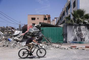 Um menino anda de bicicleta ao lado de prédios destruídos após ataques israelenses na Faixa de Gaza, na Palestina