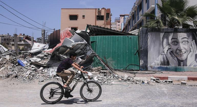 Um menino anda de bicicleta ao lado de prédios destruídos após ataques israelenses na Faixa de Gaza, na Palestina