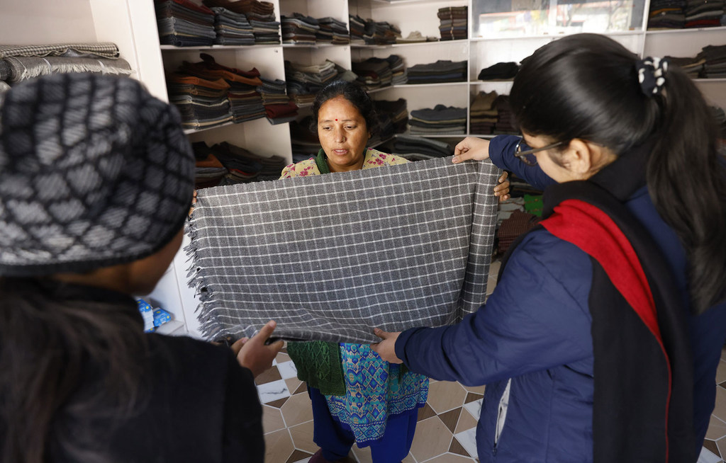 उत्तराखंड के बागोरी में एक दुकान में एक भारतीय महिला ग्राहकों को हथकरघा ऊनी कालीन दिखा रही है।
