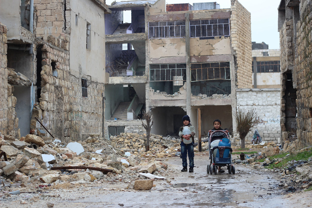 En el este de Alepo, Siria, un niño lleva un bidón de gasolina mientras otro empuja un cochecito de bebé por una calle llena de escombros de edificios dañados.