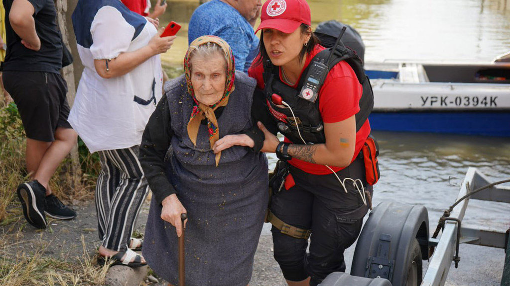Um voluntário da Cruz Vermelha da Ucrânia auxilia uma senhora idosa durante uma operação de resgate em uma área alagada perto da represa de Kakhovka.