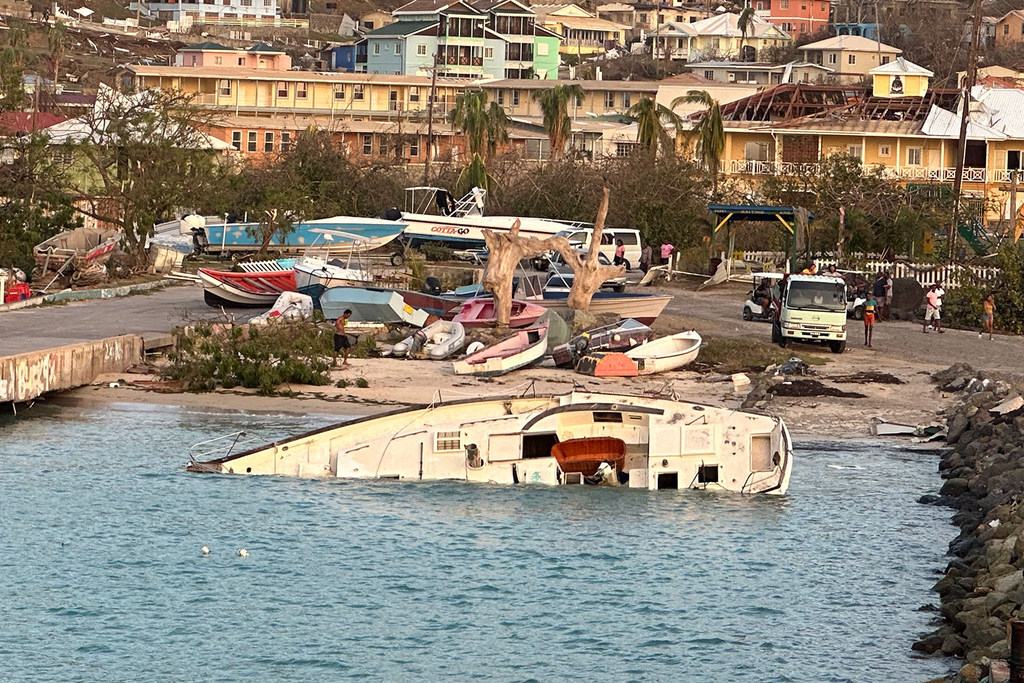 Una embarcación inundada reposa en el agua tras el paso devastado por el huracán Beryl en Union Island, San Vicente y las Granadinas, con edificios dañados y escombros al fondo.