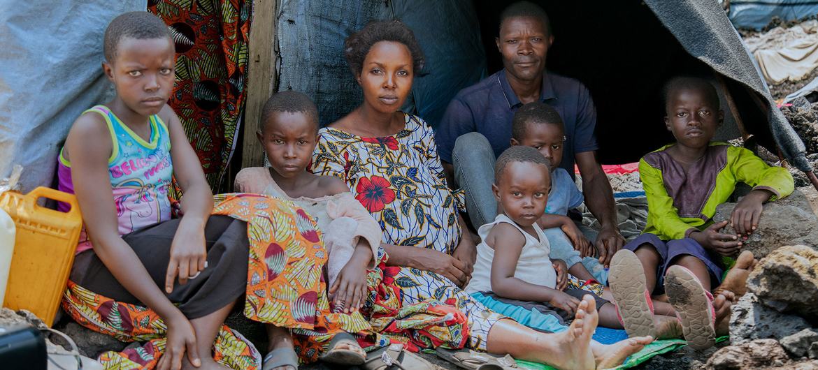 Ombeni, her husband, and their children gather outside their makeshift shelter at a displacement site west of Goma after fleeing violence. Ombeni, her husband, and their children gather outside their makeshift shelter at a displacement site west of Goma after fleeing violence.