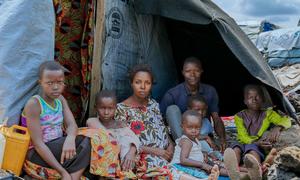 Ombeni, her husband, and their children gather outside their makeshift shelter at a displacement site west of Goma after fleeing violence.