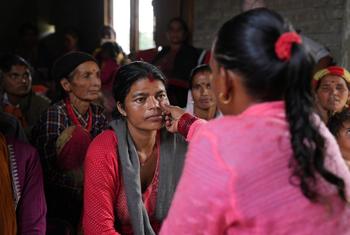A female community health volunteer screens a woman in rural nepal for anaemia by checking the lower eyelid for a pale colour.