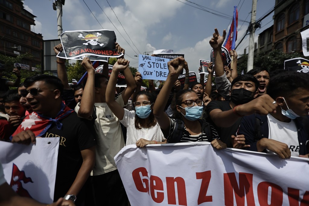 Kundi la waandamanaji vijana wa Nepal wakiwa na mabango na mabango kwenye barabara ya jiji, huku bendera moja maarufu ikiwa na maandishi 'Gen Z Move'.