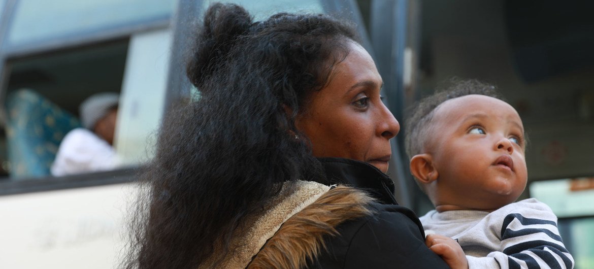 一名寻求庇护者抱着她的孩子准备登上一辆巴士，载着他们前往机场搭乘航班离开利比亚。