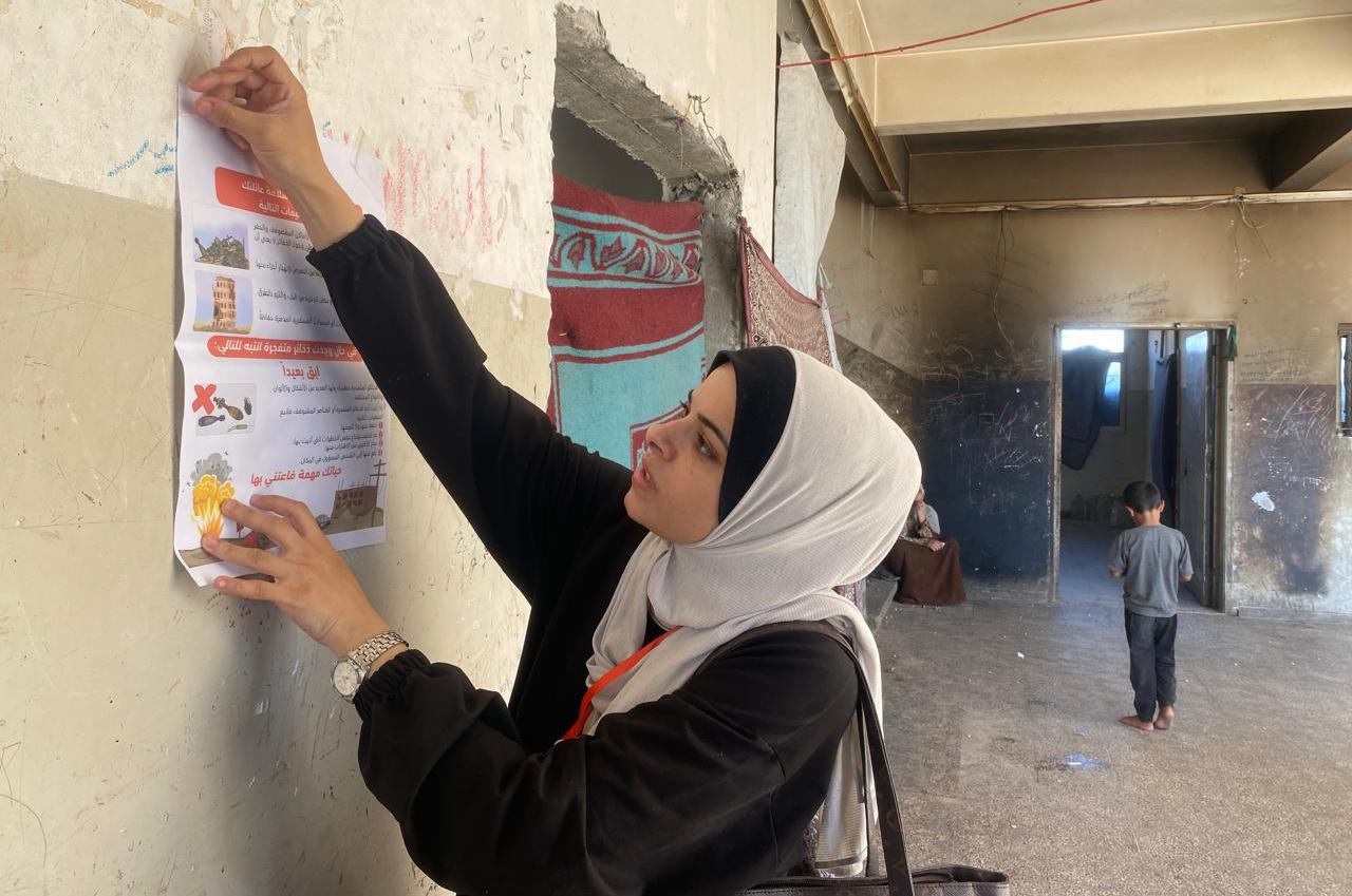 امرأة فلسطينية ترتدي الحجاب تعلق ملصقاً تعليمياً مطبوعاً على جدار في مبنى في مدينة زويدا بقطاع غزة.