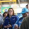 A chefe de programas da OIM, Socorro Tabosa, posa com colegas durante uma reunião em uma instalação brasileira, com uma bandeira do Brasil ao fundo.