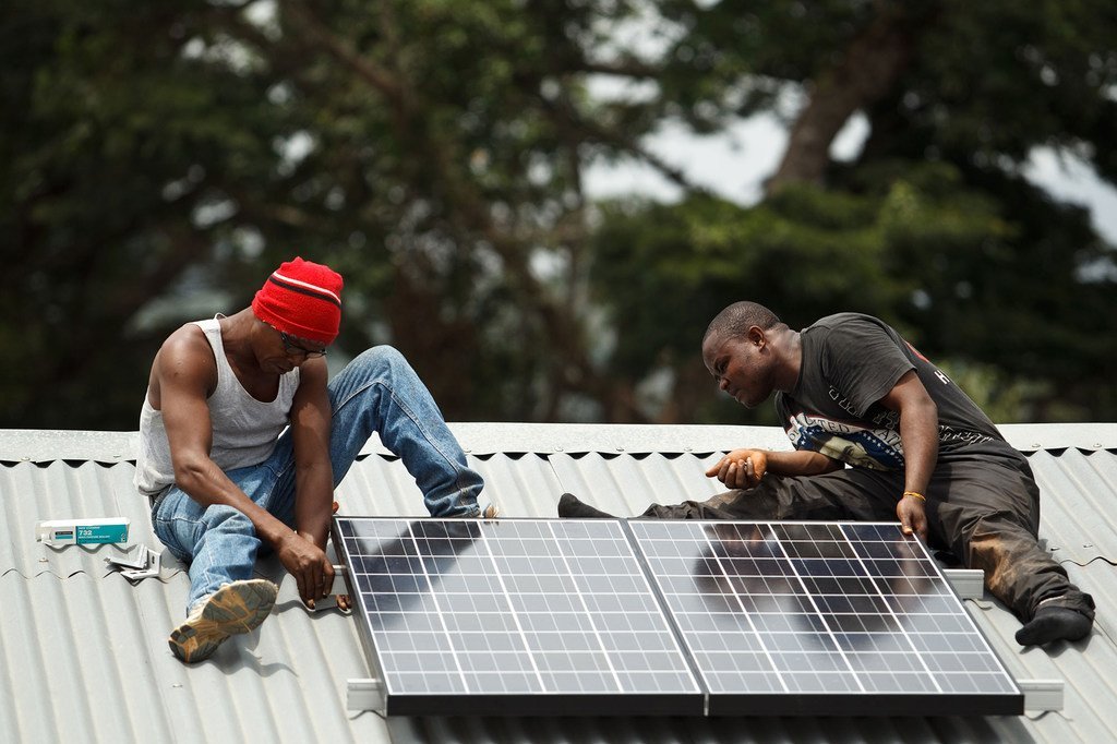 Two men install a solar panel on the roof of the Gbandiwlo Health Centre in Sierra Leone.