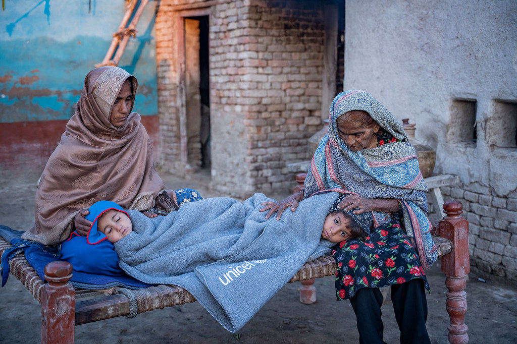 Dans un village rural, deux femmes pakistanaises enveloppent des enfants dans des couvertures de UNICEF sur un charpai.