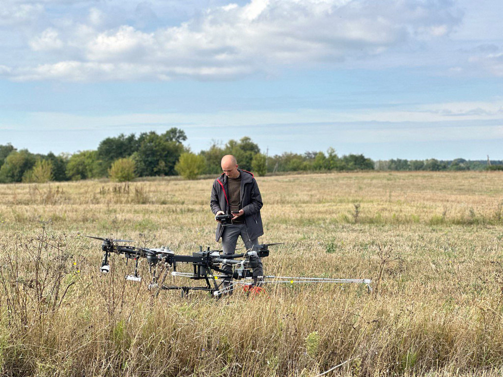A Ukrainian man operates a drone in a field for humanitarian mine action technology testing.