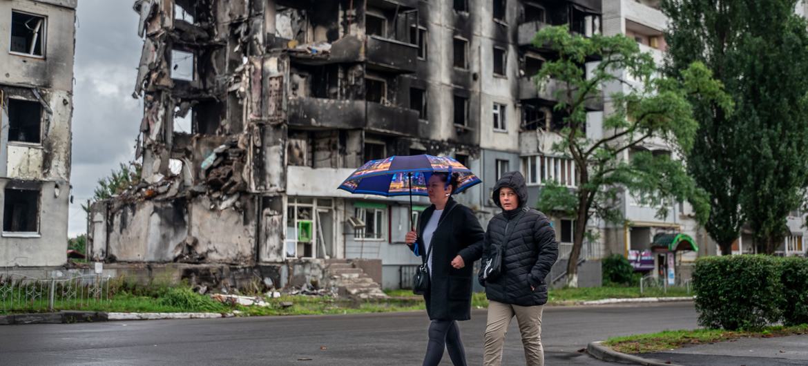 Two people walk past a destroyed residential block in the Kyiv region.