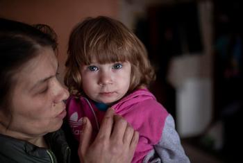 पूर्वी यूक्रेन में आंशिक रूप से नष्ट हो चुकी ऊंची इमारत में एक मां अपने बच्चे को अपने अपार्टमेंट में पकड़े हुए.