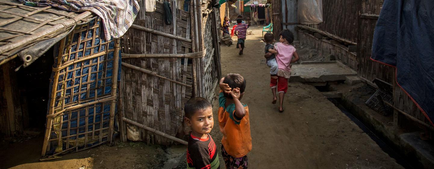 Des enfants jouent sur un chemin de terre entre des abris de fortune en bambou et en tôle dans un camp de personnes déplacées à Sittwe, au Myanmar.