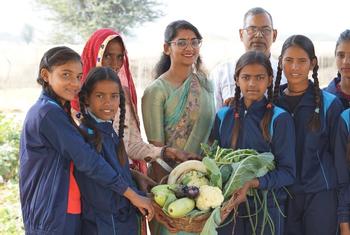 भारत में एक स्कूल के पोषण उद्यान में WFP के कर्मचारी और छात्र ताजी सब्जियों से भरी टोकरी के साथ पोज दे रहे हैं।