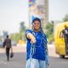 La rappeuse et militante congolaise Sista Becky pointe du doigt la caméra, vêtue d'un t-shirt et d'une casquette bleus du PAM , dans une rue de la ville.