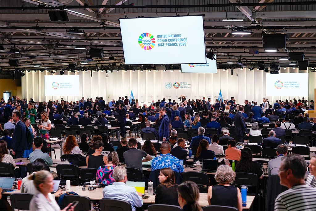 Sala plenaria de la tercera Conferencia de las ONU sobre los Océanos (UNOC3) en Niza, Francia, con numerosos asistentes sentados en mesas y una gran pantalla que muestra el logotipo de la conferencia.