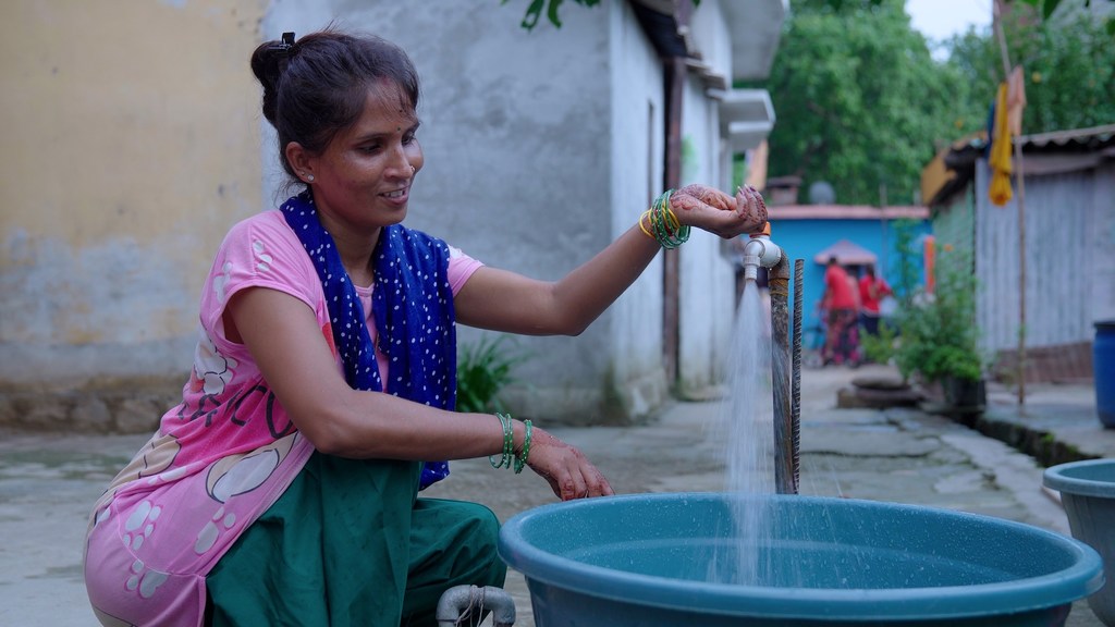 भारत के उत्तराखंड में एक महिला नए घरेलू नल के कनेक्शन से एक बेसिन में पानी भर रही है।