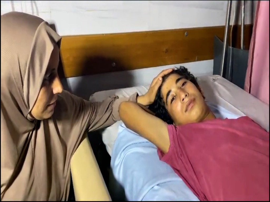 امرأة فلسطينية ترتدي الحجاب تجلس بجانب صبي صغير يرقد على سرير في المستشفى.