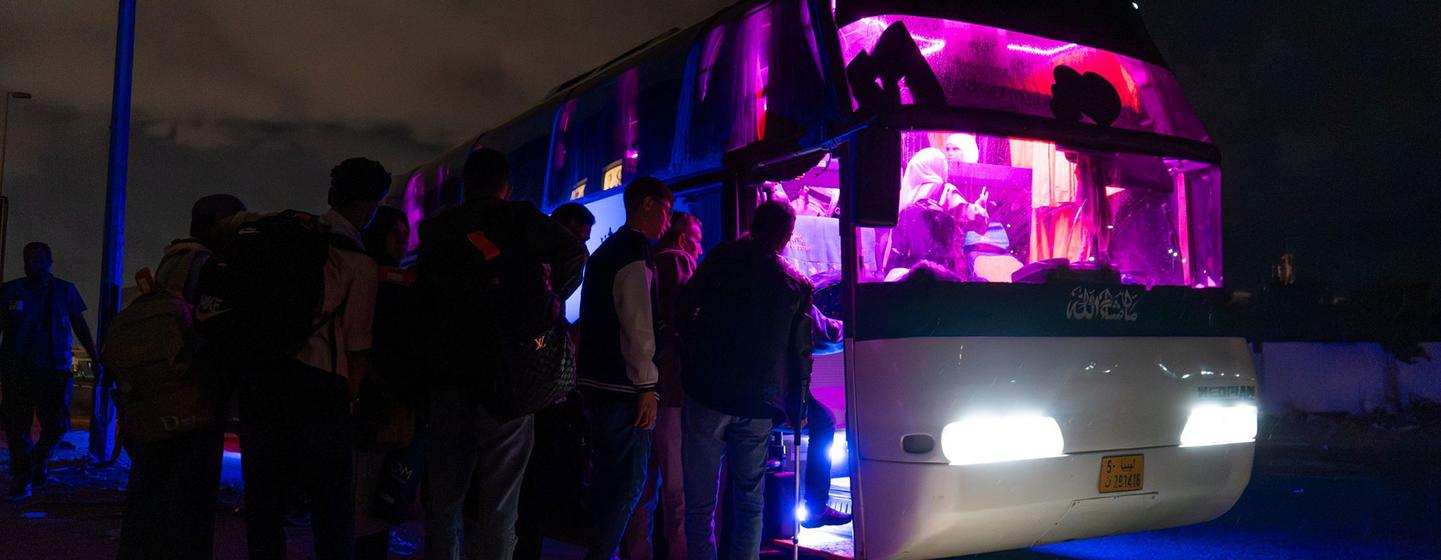 Refugiados sírios embarcam em um ônibus à noite durante um voo humanitário da OIM de Trípoli para Damasco.